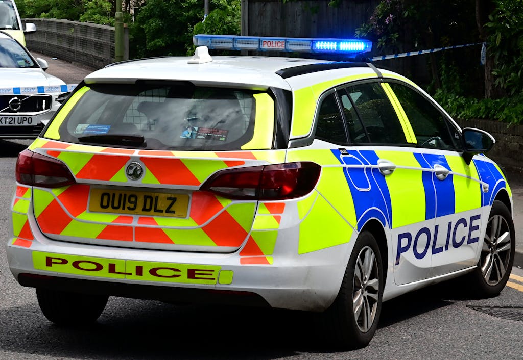 Back view of a British police car with flashing blue lights on a city road, ensuring law enforcement.